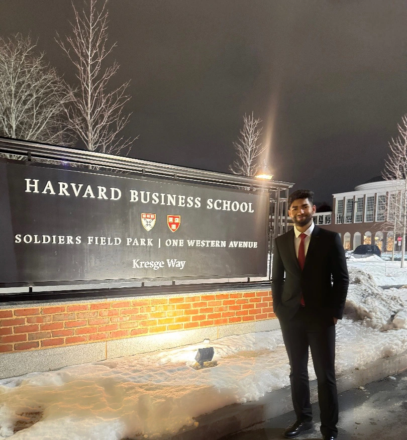 Rahul Babu — 19-year-old patent-published AI engineer and founder of Laundroswipe — at Harvard Business School, Soldiers Field Park, Kresge Way, attending Harvard HPAIR 2026 as a delegate in a dark suit and red tie.